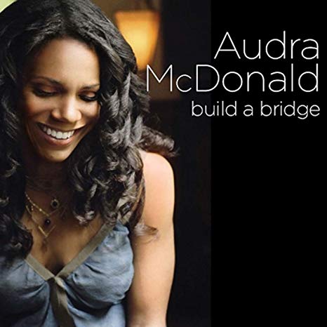 The album cover for Audra McDonald's "Build a Bridge" featuring Audra smiling and looking down against a dark background.